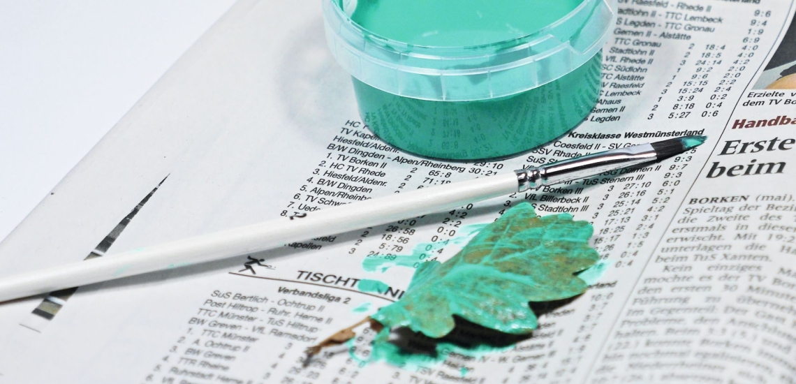 Farbe, Pinsel und mit grüner Farbe bemaltes Blatt eines Baumes