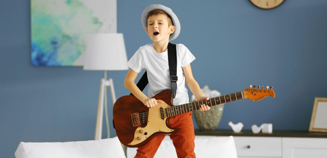 Junge singend mit E-Gitarre im Wohnzimmer