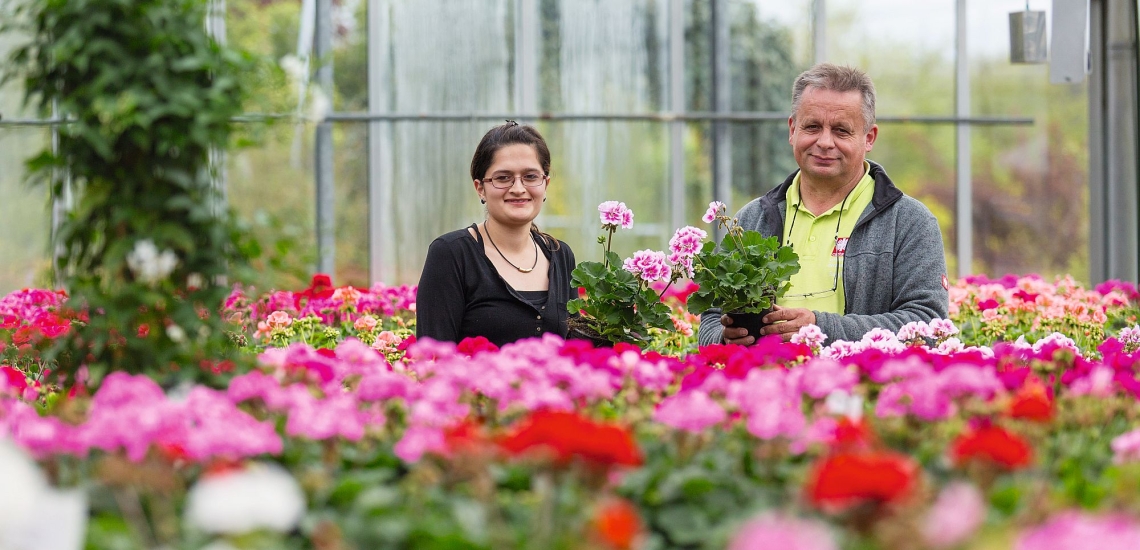 Junge Frau mit Mann hinter Blühpflanzen 