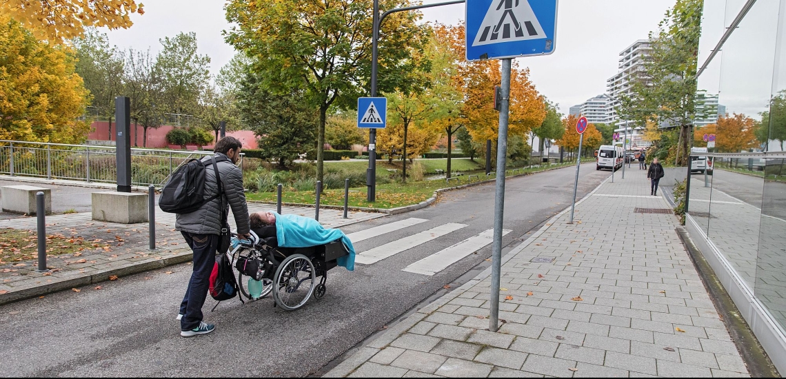Alexander Greis im Rollstuhl mit Betreuer auf der Straße