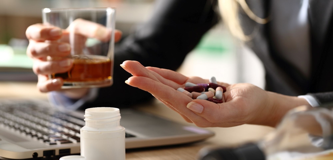 Frau am Schreibtisch mit Alkohol und Tabletten