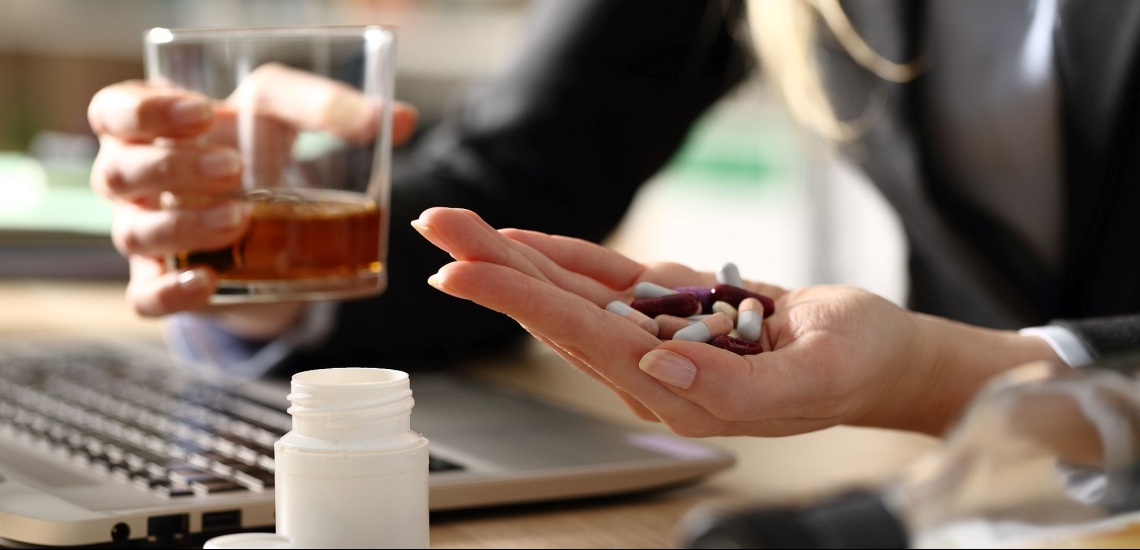 Frau am Schreibtisch mit Alkohol und Tabletten