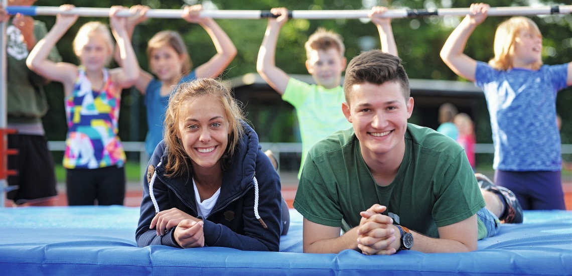 Zwei Jugendliche liegen auf Sportmatte und lachen in die Kamera 