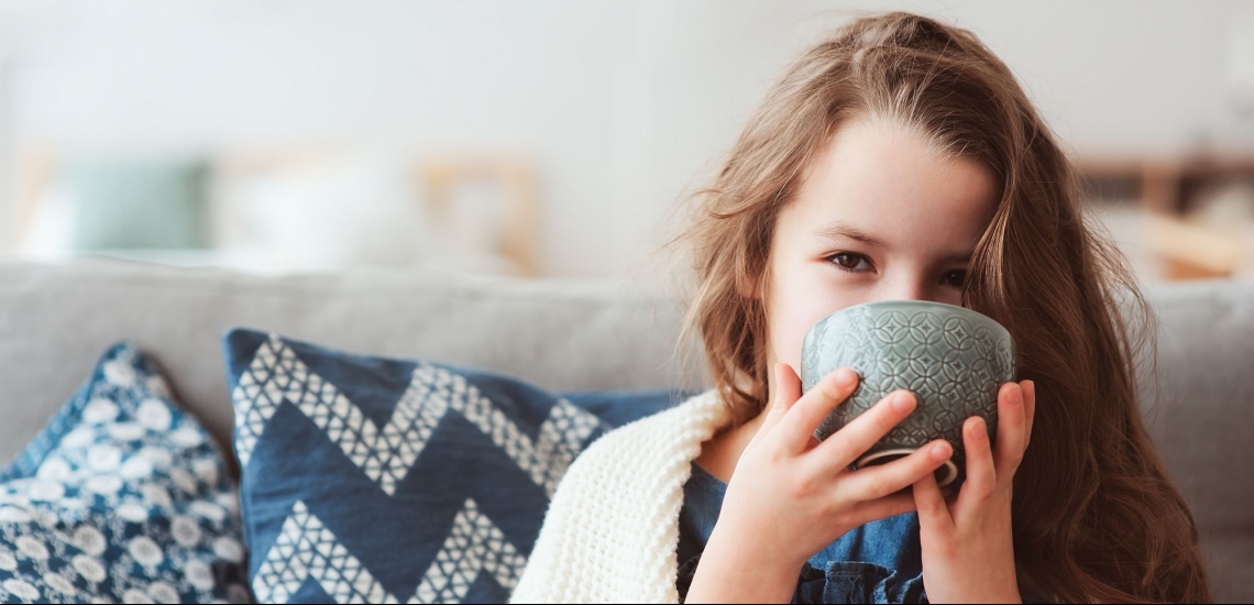 Mädchen auf Sofa mit Decke trinkt Tee 