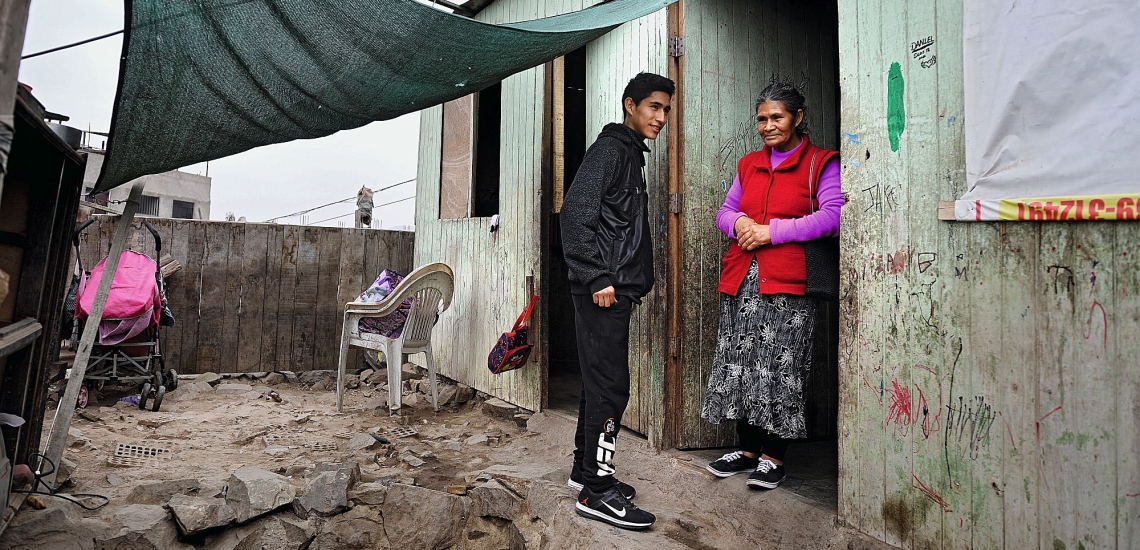 Jugendlicher mit seiner Großmutter vor einfachem Holzhaus 
