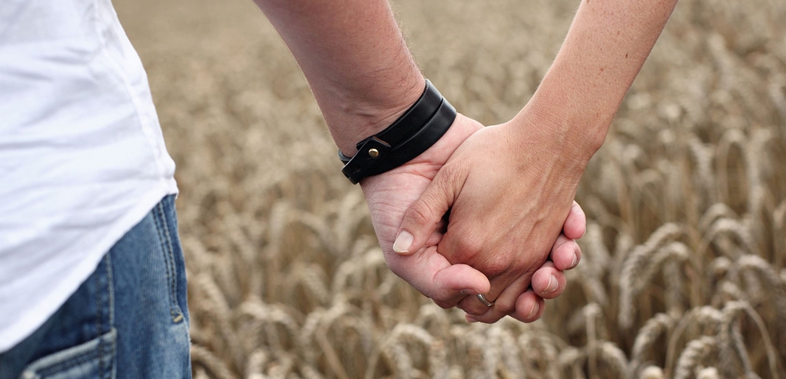 Ineinander gelegte Hände eines Paares vor Kornfeld 