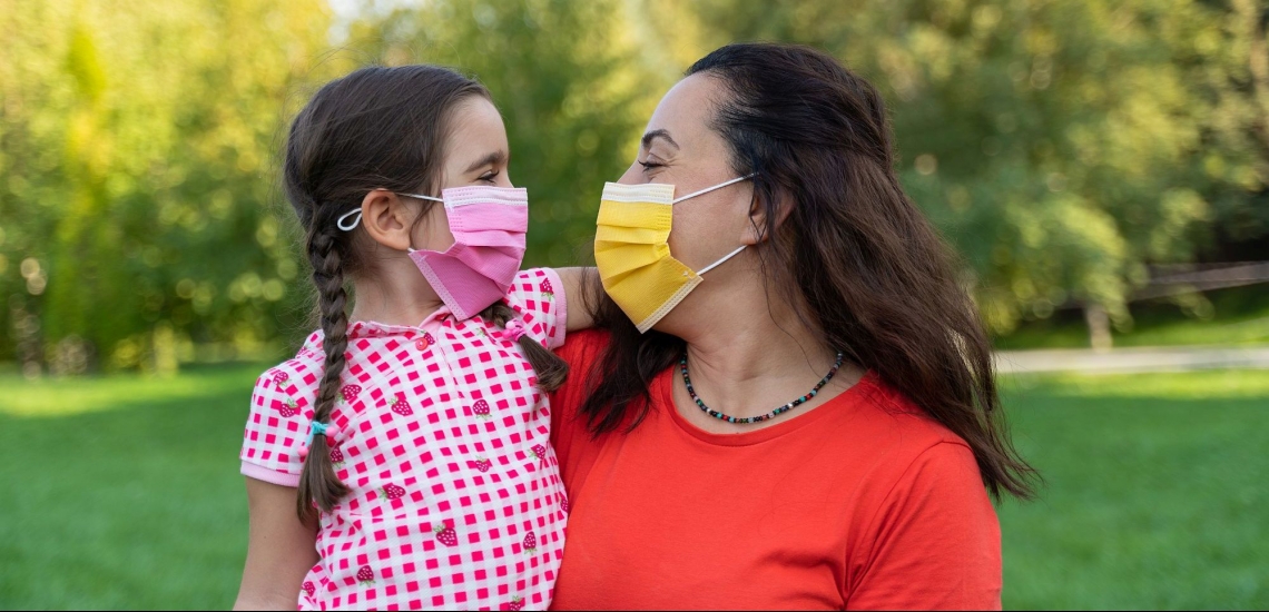 Mutter und Tochter lachend mit Masken auf Wiese 