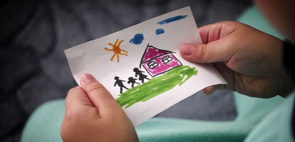 Kinderhände mit Zeichnung von Familie und Haus 