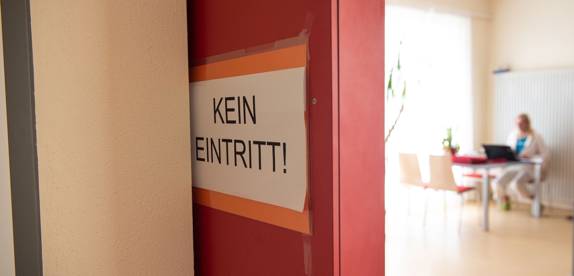 Schild Kein Eintritt! dahinter Raum mit Frau am Schreibtisch 