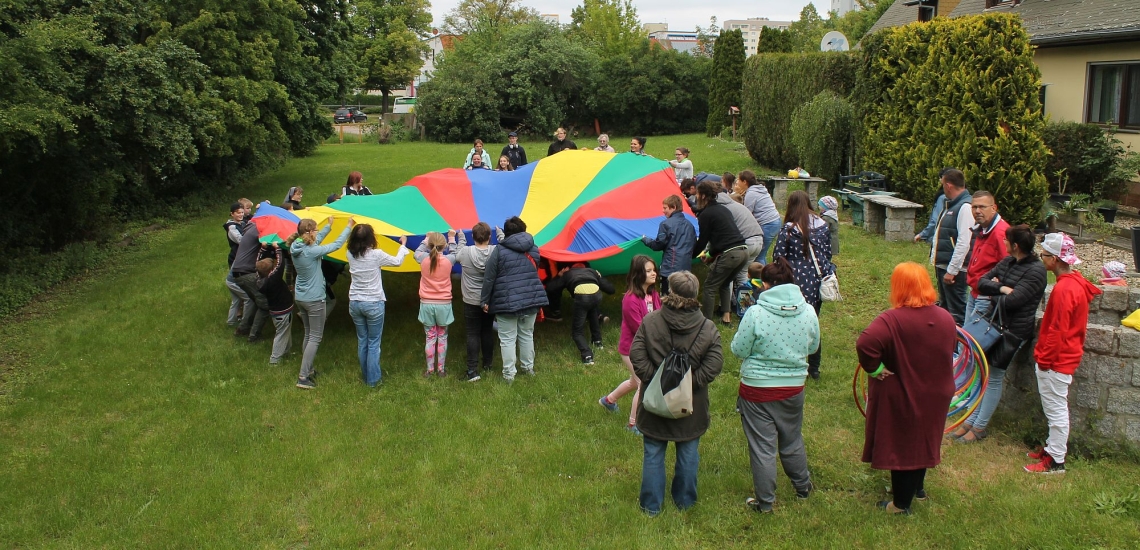Kinder und Erwachsene im Garten mit großem bunten Tuch