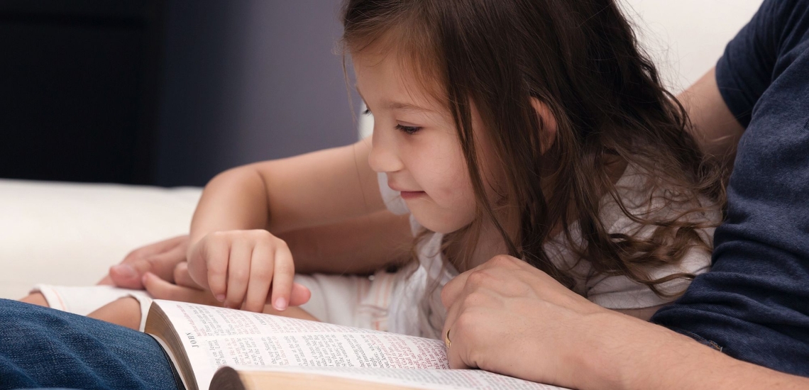 Mädchen liest mit Vater in Bibel 