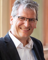 Porträt Mann mit graumelierten Haaren, Brille und Anzug lachend