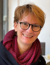 Porträt einer Frau mit kurzen hellbraunen Haaren, Brille und lila Schal