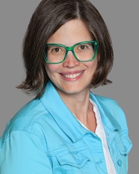 Barbara Humer - Brünette Frau mit hellblauem Hemd und grüner Brille