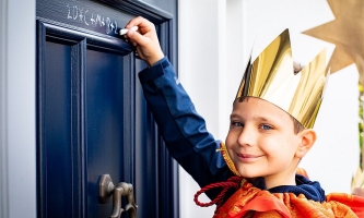 Sternsinger mit goldener Krone schreibt mit Kreide den Segen an eine Haustür