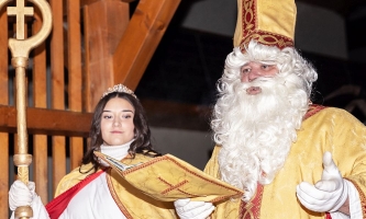 Als Bischof Nikolaus kostümierter Mann liest aus goldenem Buch, daneben eine Frau im Engelskostüm, die den Bischofsstab hält.