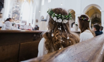 Erstkommunionkinder in festlicher Kleidung sitzen während des Gottesdienstes in einer Kirchenbank