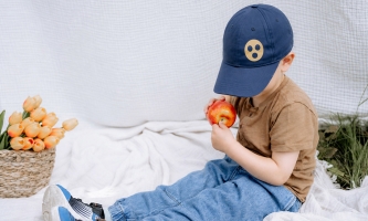 Ein Kind mit einer Baseballkappe mit Blindenzeichen betastet einen Apfel