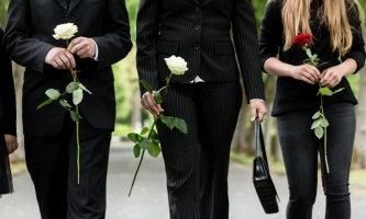Menschen in Trauerkleidung laufen in einer Reihe mit Rosen auf dem Friedhof