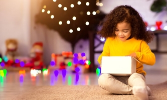 Kind vor Weihnachtsbaum schaut in Geschenkpaket und freut sich