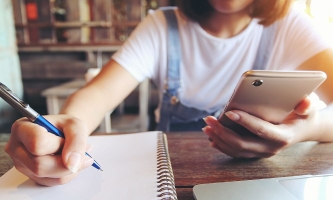 Jugendliche am Tisch mit Smartphone, Laptop, Notizblock und Stift