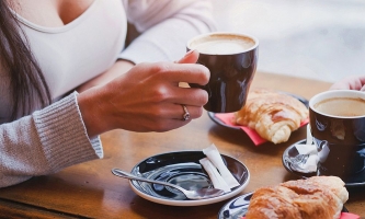 Tisch mit Kaffeetassen und Croissants, Hände und Oberkörper von zwei Frauen, die am Tisch sitzen