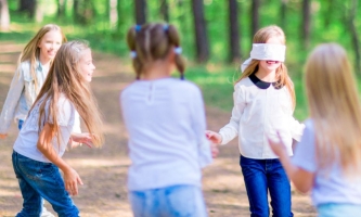 Fünf Mädchen spielen draußen, eins hat eine Augenbinde