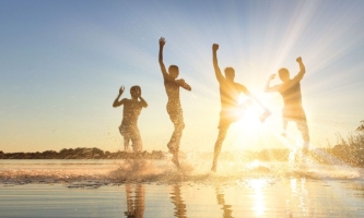 Jugendliche springen am See in der untergehenden Sonne im Wasser herum
