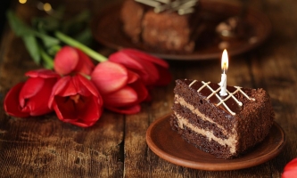 Kaffeetafel mit einen Stpck Schokoladenkuchen und brennender Kerze und auf dem Tisch liegenden roten Tulpen
