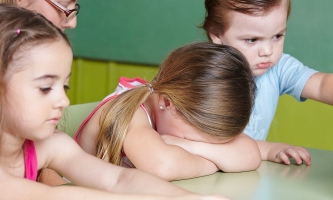 Kind weint in Kita, daneben andere Kinder und Erzieherin