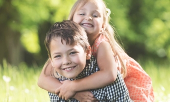 Zwei Kinder lachend im Grünen, Junge trägt Mädchen auf dem Rücken