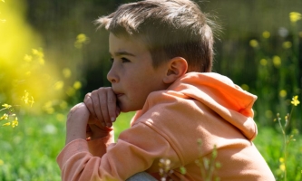 Junge sitzt nachdenklich im Gras in der Sonne