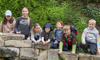 Kinder lehnen lachend in einer Reihe über einer Natursteinmauer auf dem Gelände des Klosters Ensdorf