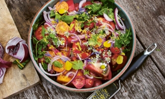 Tomatensalat mit Zwiebeln, Kräutern und Blüten in Schale auf Holztisch