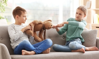zwei Geschwister sitzen auf einem Sofa und ziehen an einem Stoffhasen
