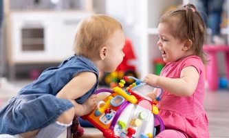 Ein kleines Mädchen nimmt einem anderen ein buntes Plastikspielzeug weg