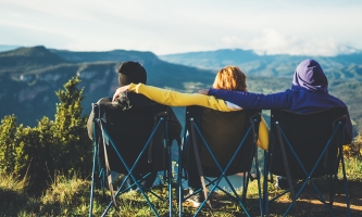 Drei Personen sitzen auf drei Klappstühlen in den Alpen und schauen in die Ferne