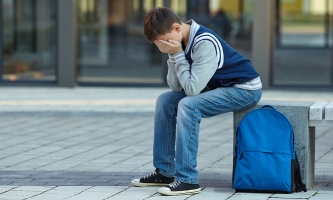 Junge sitzt auf einer Bank und hat die Hände vors Gesicht geschlagen