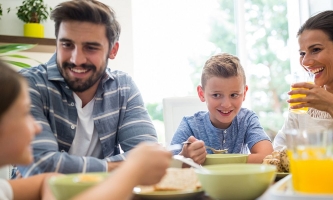 Vater, Mutter und zwei Kinder sitzen lachend am gemütlichen Frühstückstisch