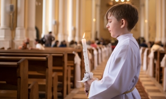 Erstkommunion - Junge mit Kerze im Mittelgang einer Kirche