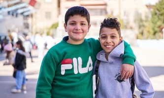 zwei Jungen lachen mit umeinander gelegten Armen in die Kamera