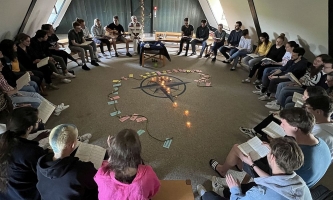 Viele Jugendliche sitzen im Kreis auf Stühlen, in der Mitte Kerzen und eine Schnur mit beschrifteten Zetteln