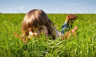 Kind liegt auf dem Bauch im Gras und schaut zwischen den Grashalmen durch