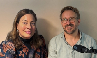 Julia Dahmen und Christian Pröls-Geiger lächeln in die Kamera. Am unteren rechten Bildrand ist ein Mikrofon zu sehen.