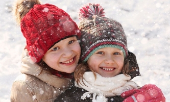 zwei Kinder lachend mit Winterkleidung im Schnee
