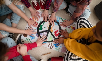 Hände von Jugendlichen liegen auf einem Plakat, auf dem ein Peace-Zeichen gemalt ist und bunte Handabdrücke zu sehen sind.