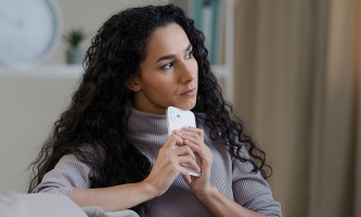 Frau hält Handy in der Hand und schaut nachdenklich und zweifelnd