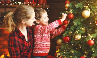 Ein Mädchen schmückt zusammen mit seiner Mutter einen Christbaum