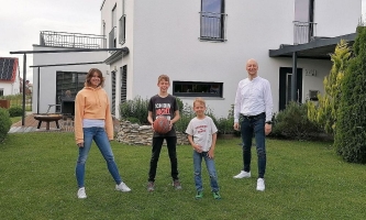 Vater, Mutter und zwei Kinder lachend vor großem Haus im Garten