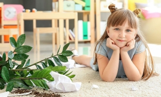 Kind liegt auf dem Boden neben einer umgekippten Topfpflanze mit Erde und Papier
